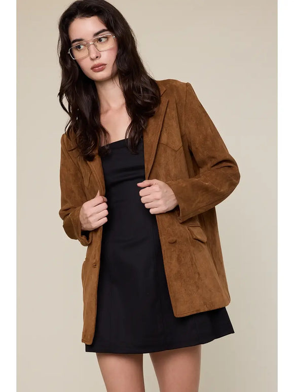 Woman wearing a brown suede jacket over a black dress against a beige background