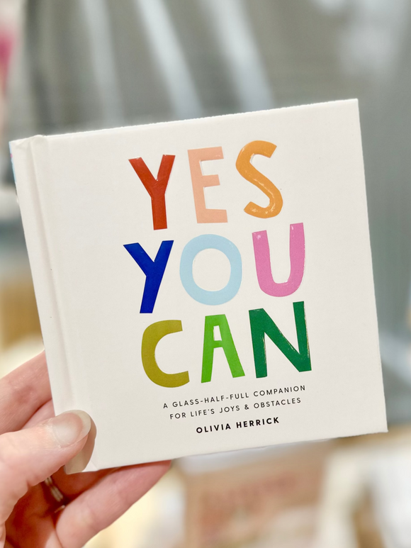 Book titled 'YES YOU CAN' held by a person with a blurred background