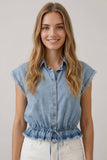 Woman wearing a light blue denim sleeveless shirt against a plain background