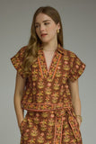 A woman modeling a brown short-sleeve wrap dress with a yellow and orange floral block print, paired with tan cowboy boots, against a solid gray studio background.